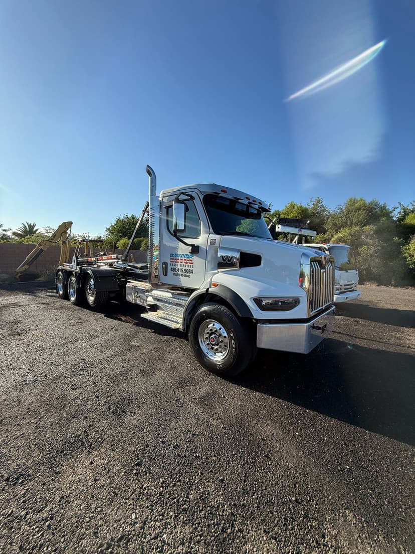 White heavy-duty truck parked on gravel, with clear blue sky and trees in the background.