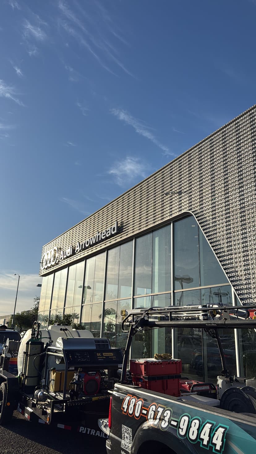 Audi Arrowhead dealership with clear blue sky and parked service vehicles in foreground.