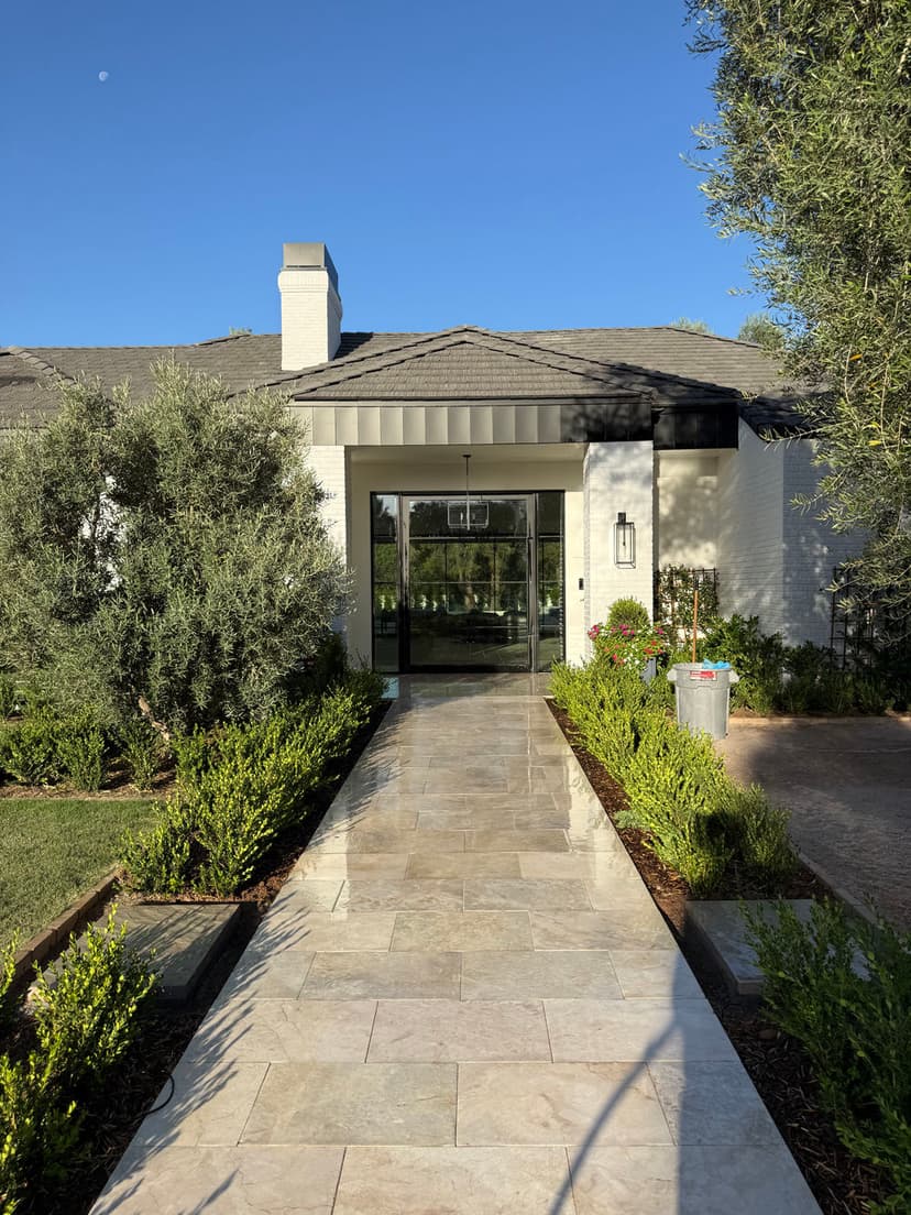 Modern home entrance with a stone pathway, greenery, and clear blue skies.