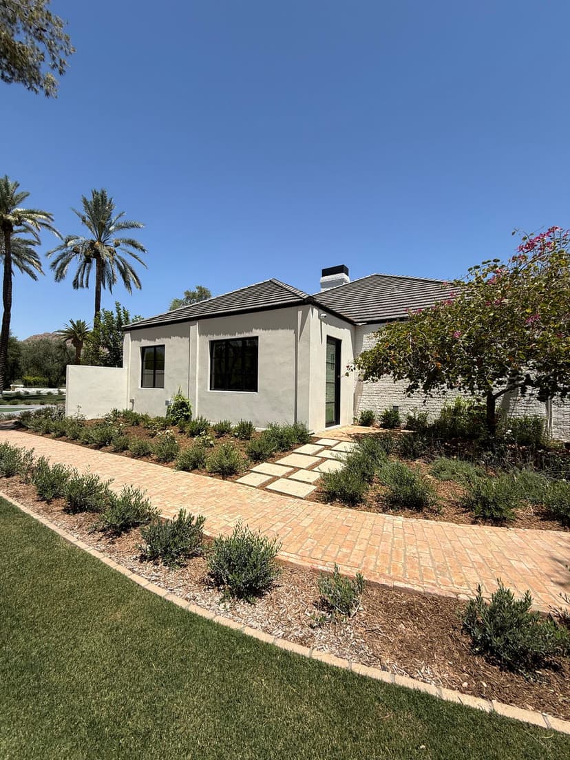 Modern home exterior with landscaped garden and pathway, surrounded by palm trees and greenery.