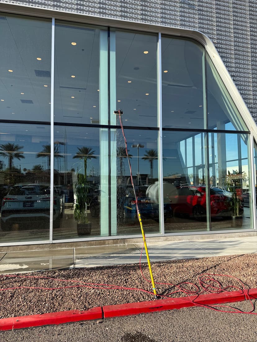 Power washing a commercial building's large glass windows with a water pole and hose.