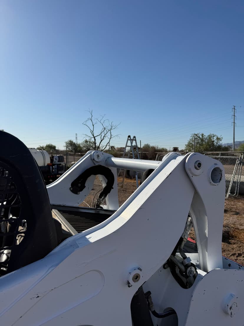 Close-up of a white excavator arm with clear blue sky and background equipment.