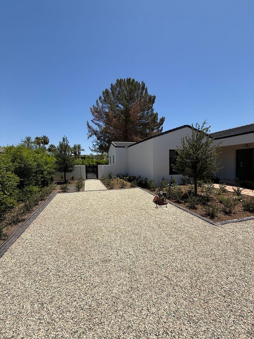 Modern house entrance with gravel driveway and landscaped garden under clear blue sky.